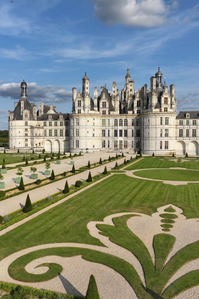 A breathtaking view of Château de Chambord with its meticulously designed French gardens. The castle’s intricate turrets and spires contrast against a bright blue sky.