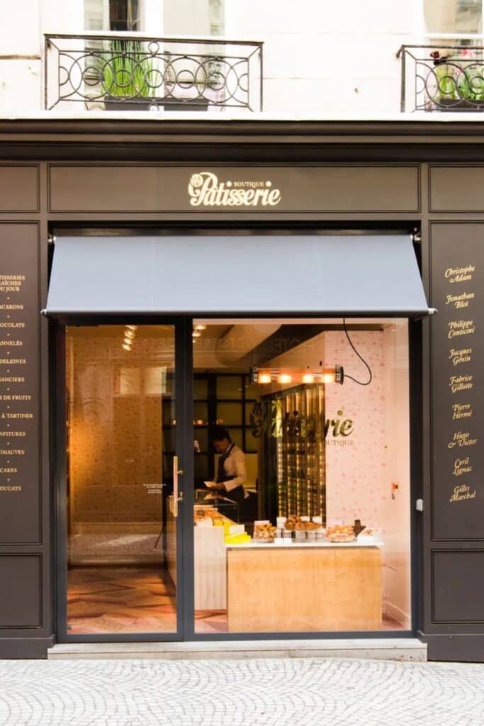 The chic storefront of Fou de Pâtisserie on Rue Montorgueil, a boutique pastry shop showcasing some of Paris’s best pâtisserie creations. Through the glass, an elegantly designed interior and an employee preparing treats can be seen.