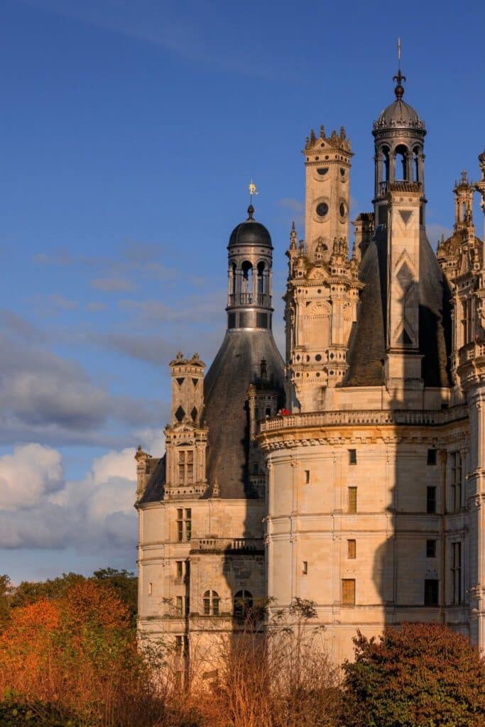 A close-up of the castle’s turrets and towers illuminated by warm sunlight. The detailed stonework and unique French Renaissance architecture stand out against a deep blue sky.