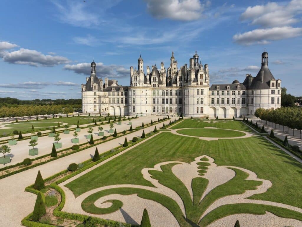 A wide-angle view of Château de Chambord’s symmetrical gardens, featuring ornate hedges and gravel paths leading towards the magnificent castle.
