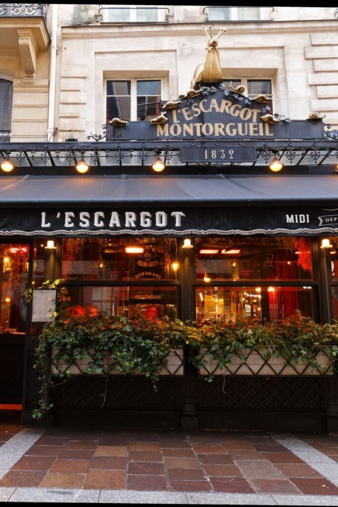 The iconic façade of L’Escargot Montorgueil, a historic Parisian restaurant known for its escargots. The black awning and golden snail sculptures above the sign add to its classic French charm.