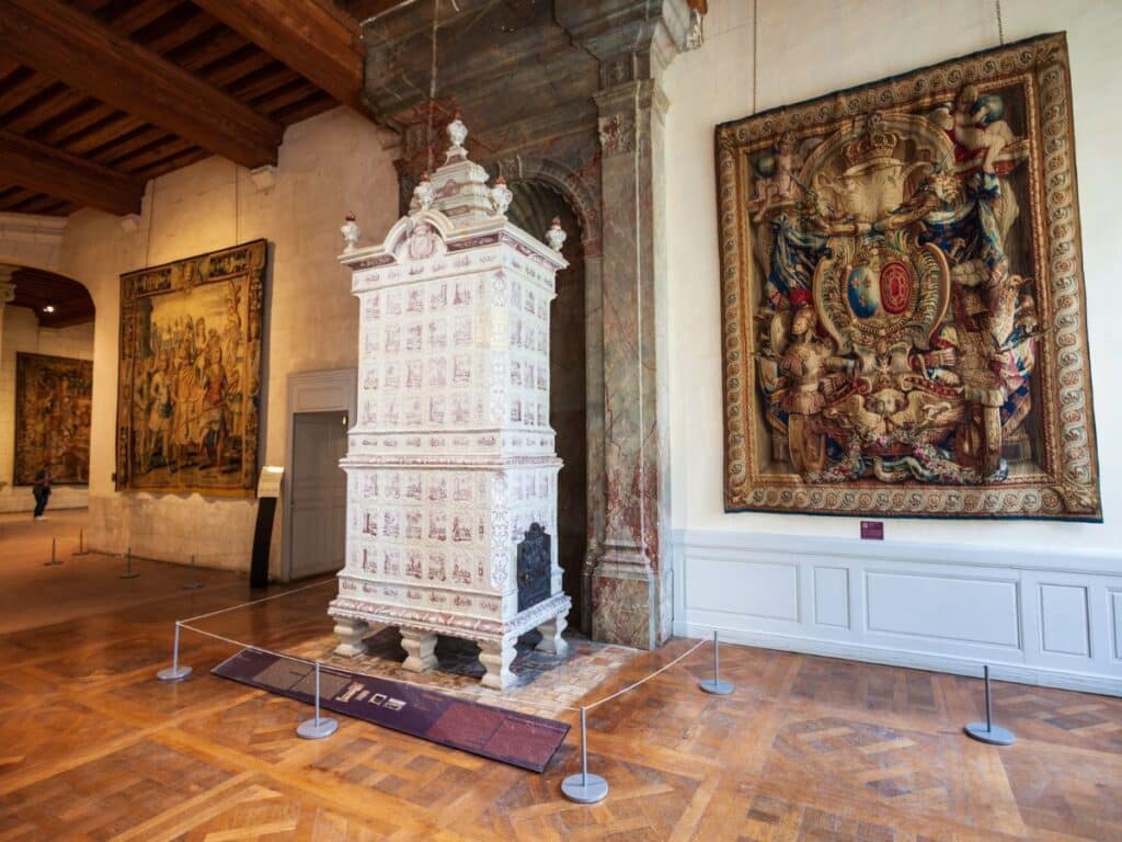 A grand interior in Château de Chambord, featuring an ornate tiled stove, detailed tapestries, and rich wooden beams. The space highlights the castle’s Renaissance influence.