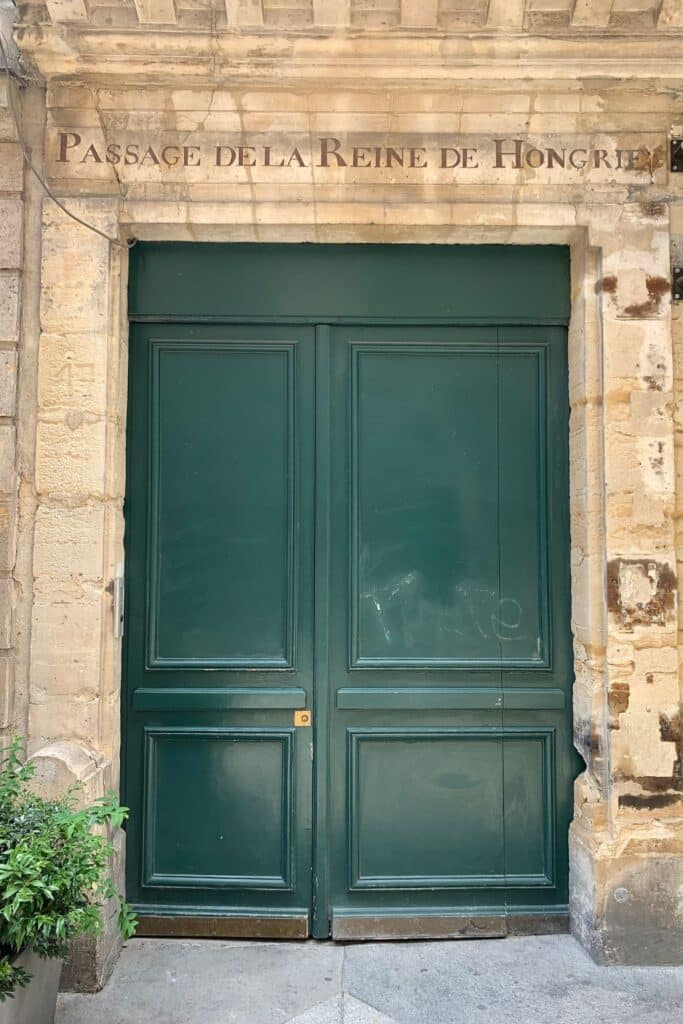 A set of grand dark green doors with the inscription "Passage de la Reine de Hongrie" above, marking a historic passageway on Rue Montorgueil. The aged stone walls give it an old-world Parisian feel.