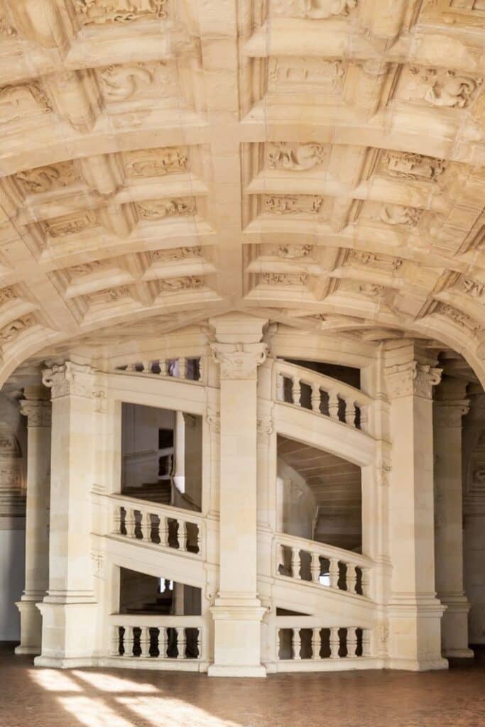 The legendary double-helix staircase inside Château de Chambord, with its intricate balustrades and sculpted ceiling, bathed in natural light from surrounding archways.