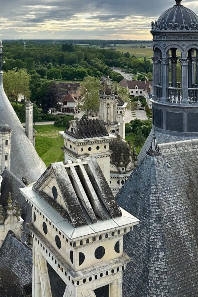 A striking perspective from Château de Chambord’s rooftop, showcasing its ornate chimneys, towers, and slate-tiled domes overlooking the lush French countryside.