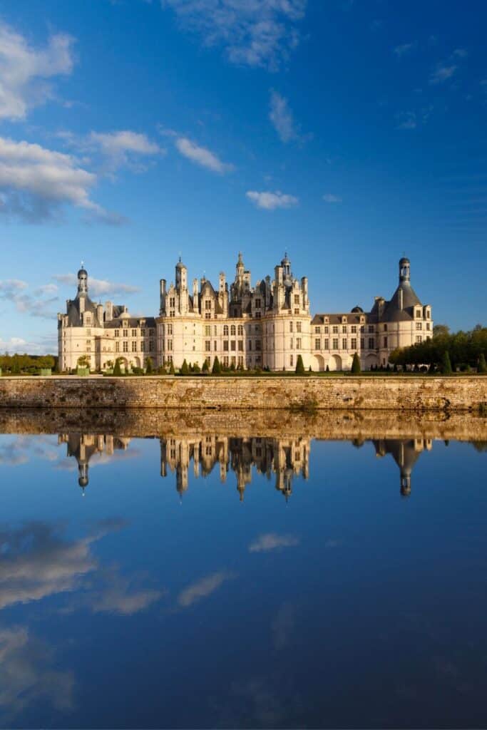 A mesmerizing reflection of Château de Chambord in a tranquil body of water, with its elaborate spires and turrets mirroring the deep blue sky.