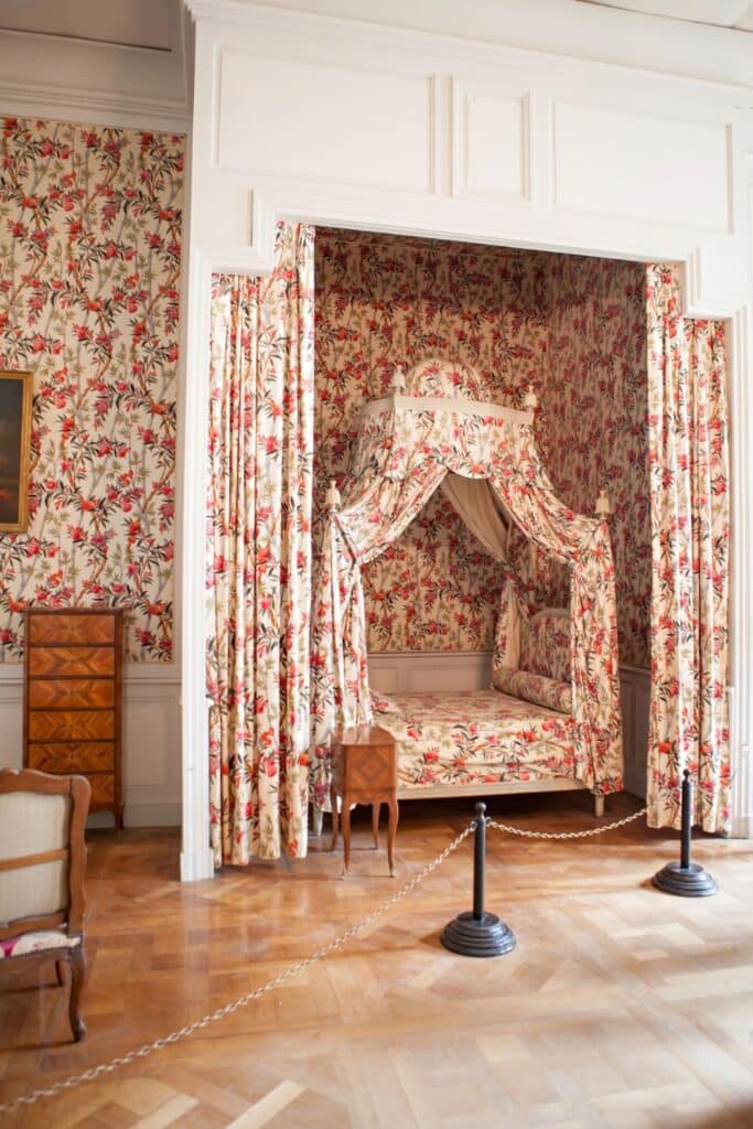 A charming bedroom in Château de Chambord with floral-patterned wallpaper and matching fabric canopy bed, evoking a cozy yet aristocratic ambiance.
