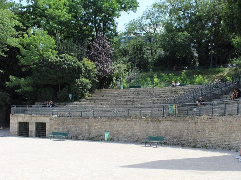 Stone seating of the Arènes de Lutèce in Paris’ Latin Quarter, a preserved Roman amphitheater nestled among trees with scattered visitors enjoying the sunny day. This hidden historic gem is a peaceful contrast to the lively streets of the Latin Quarter.
