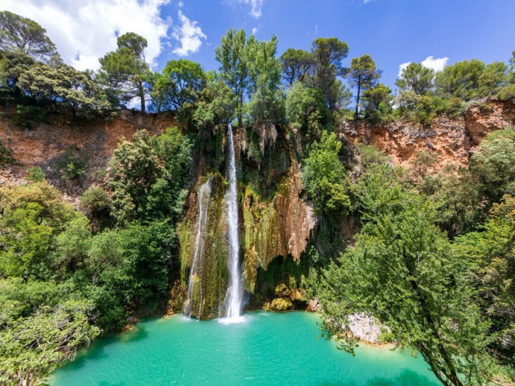 The Cascade de Sillans waterfall cascading into a turquoise pool, surrounded by rocky cliffs and dense forest, showcasing the natural beauty of the South of France.