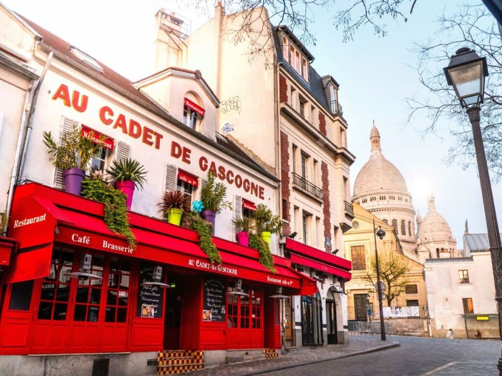 Vibrant red facade of Au Cadet de Gascogne café and brasserie in Montmartre, near the Sacré-Cœur Basilica. A historic haunt for famous residents of Montmartre like Toulouse-Lautrec and other artists of the Belle Époque.