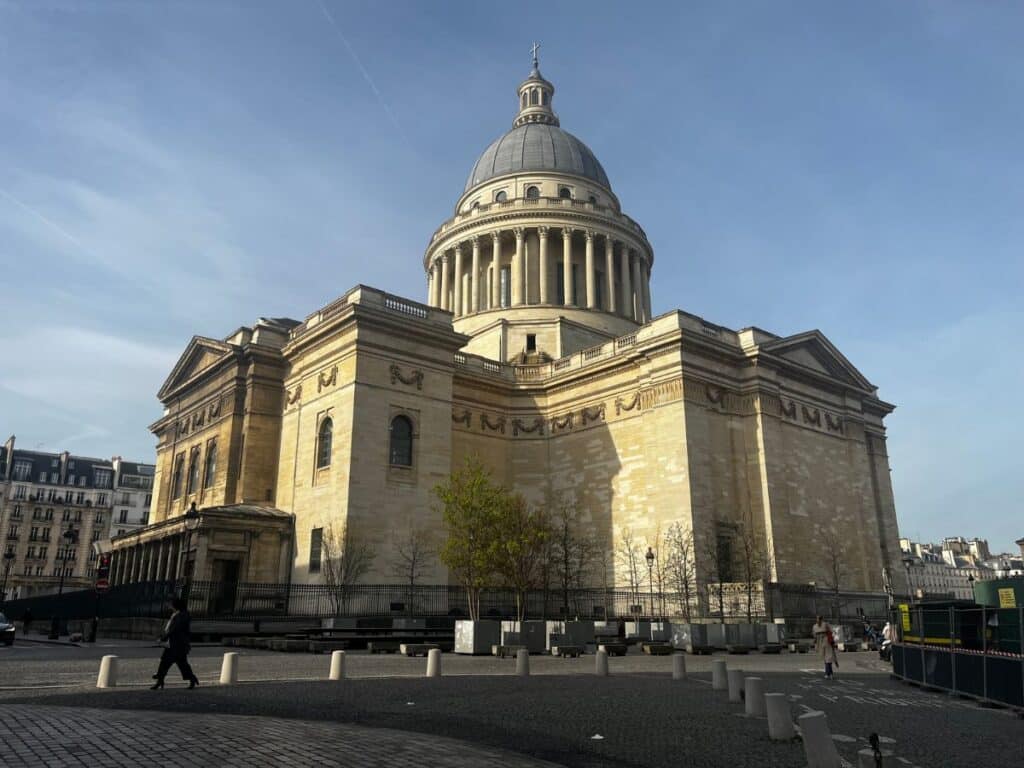 The grand neoclassical Panthéon in Paris’ Latin Quarter under a clear blue sky, its iconic dome and columns dominating the cobblestone square below. A landmark rich in history, it's one of the Latin Quarter’s most striking architectural icons.