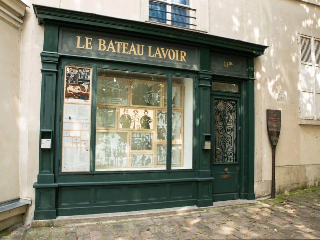 Entrance to Le Bateau-Lavoir, a legendary Montmartre studio building that housed famous residents like Pablo Picasso and other avant-garde artists. The green storefront displays historical photos and artwork tied to the building’s rich artistic history.