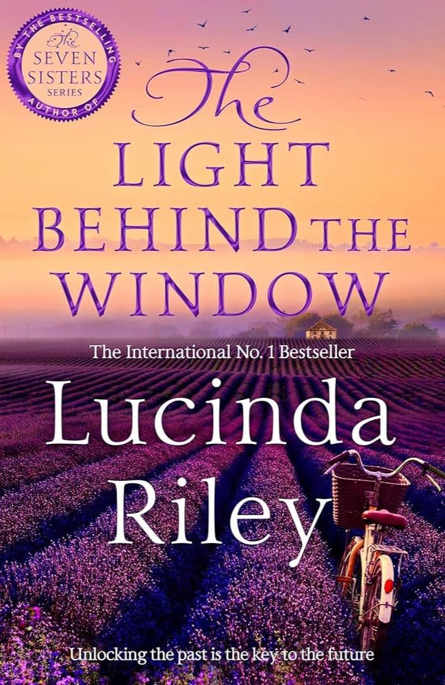 Book cover of The Light Behind the Window by Lucinda Riley, featuring a lavender field at sunset with a vintage bicycle in the foreground—an atmospheric choice among summer beach reads set in France.