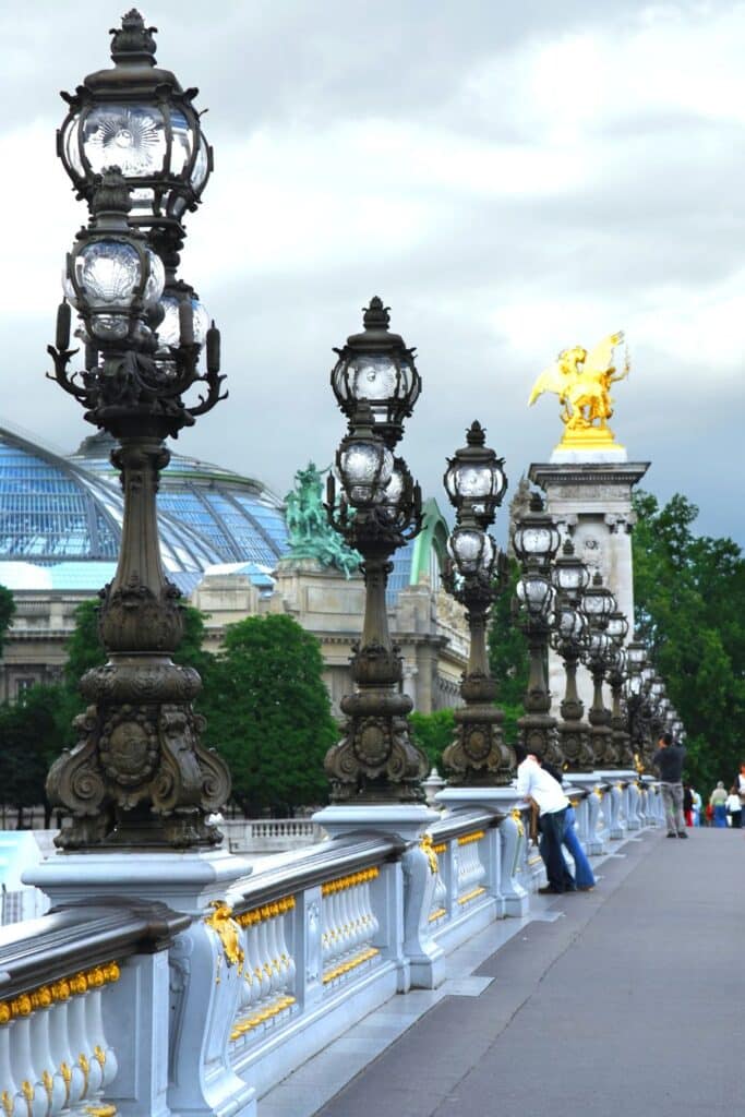 View of the ornate lampposts and golden statue on Pont Alexandre III, one of the most extravagant bridges in Paris, with the Grand Palais visible in the background.