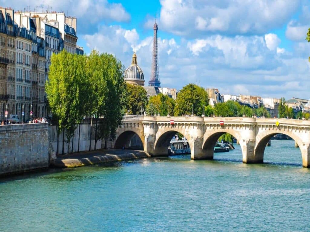 Pont Marie arches across the Seine, framed by lush trees and Haussmann-era buildings, with the Eiffel Tower in the distance. It’s one of the oldest bridges in Paris still in use today.