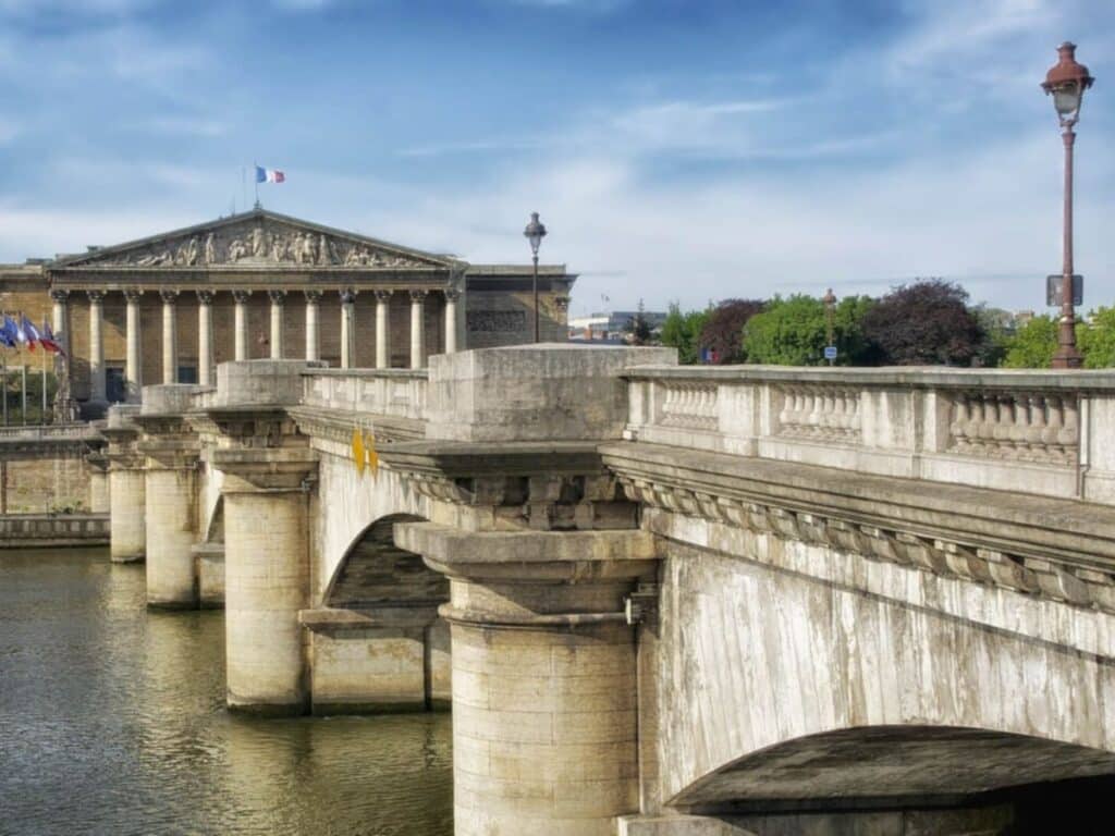 Pont de la Concorde stretches across the Seine toward the National Assembly building, marked by French flags and neoclassical columns. It’s one of the key bridges in Paris linking historic government sites.