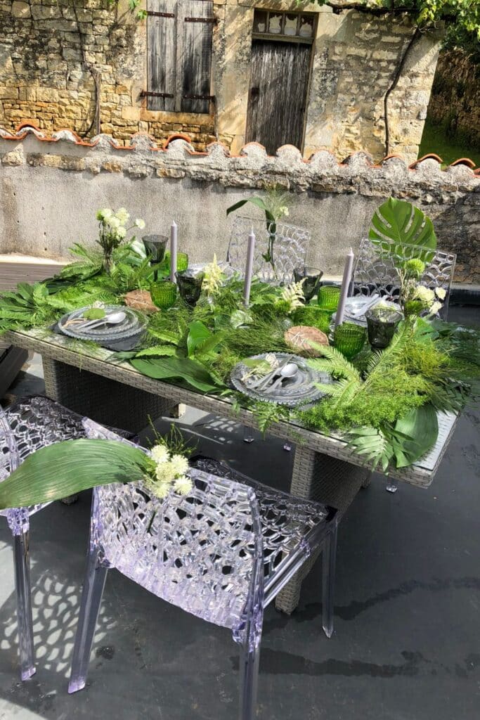 A full view of the decorated table, featuring layered greenery, crystal-clear chairs, and natural textures. The mix of modern acrylic furniture and organic elements creates a chic yet earthy aesthetic.
