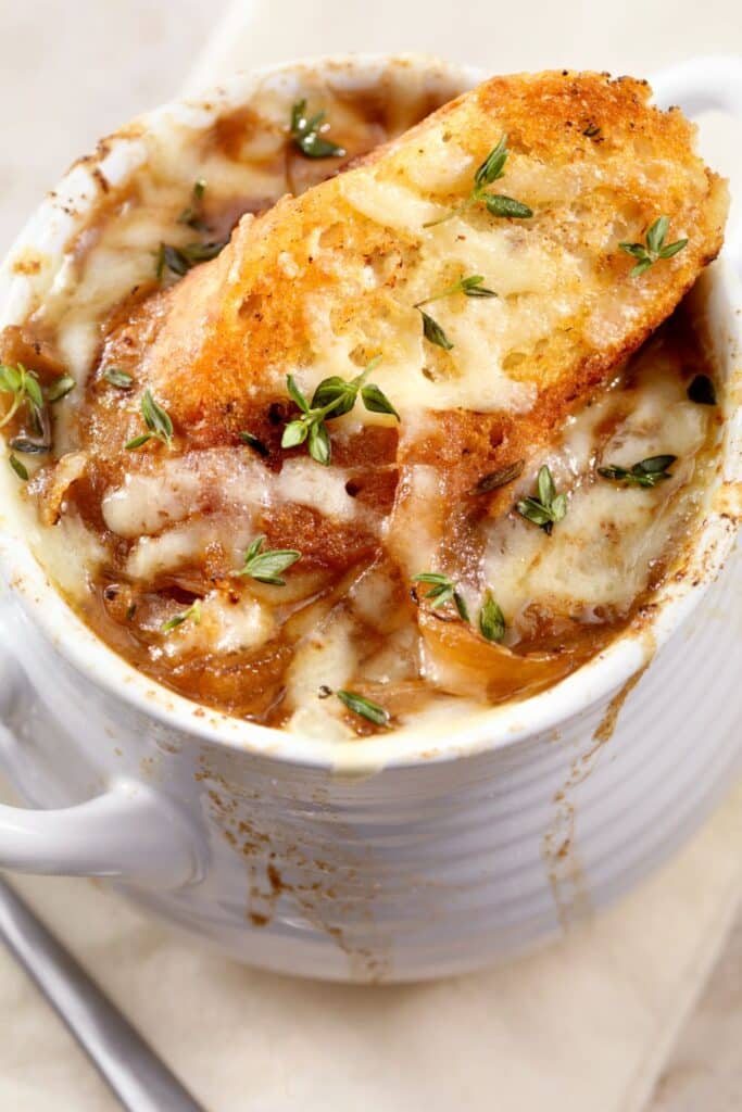 Hot bowl of French onion soup topped with golden melted cheese, toasted baguette slice, and fresh thyme, bubbling over with rich caramelized onion flavor.