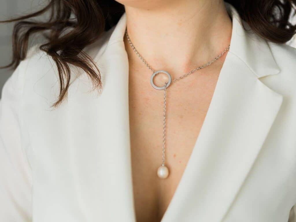 Close-up of a woman in a white blazer wearing a delicate silver lariat necklace with a pearl drop, showcasing the minimalist elegance central to Parisian chic.