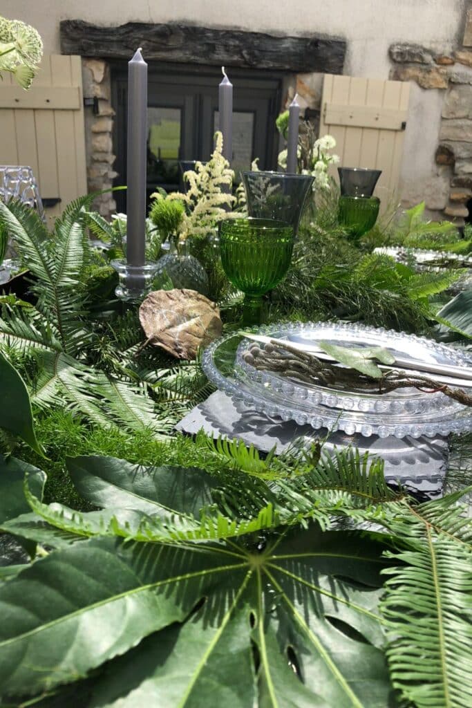 A side view of the table adorned with tall gray candles, delicate flowers, and an abundance of green foliage. The soft candlelight enhances the organic, nature-inspired decor.