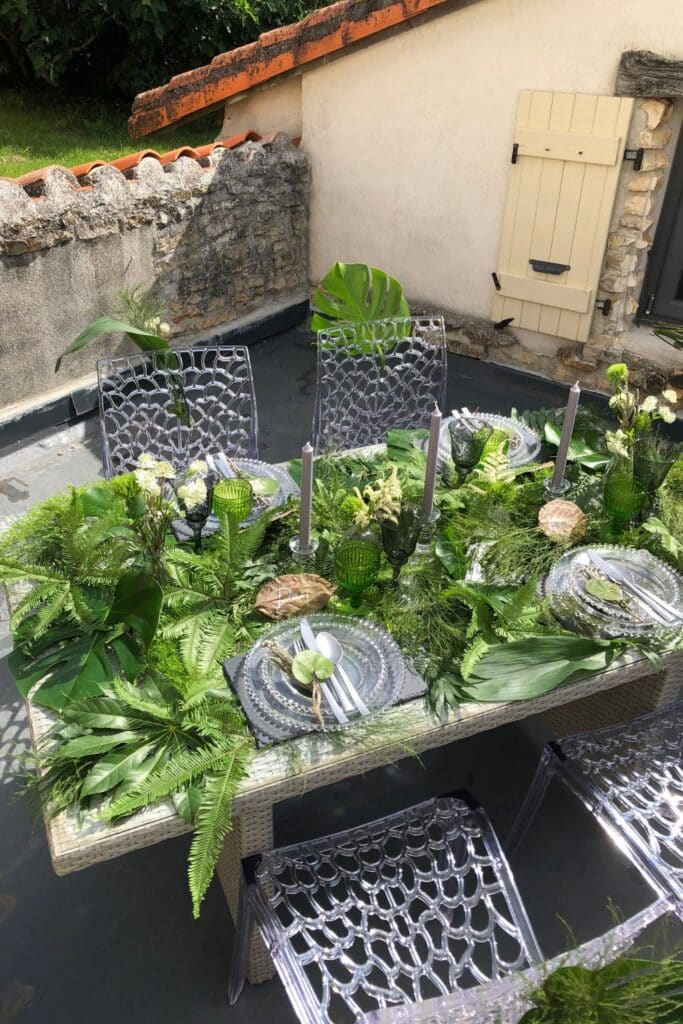 A naturally styled summer tablescape set for an al fresco meal. The clear acrylic chairs, green glasses, and lush foliage create a fresh and elegant atmosphere.