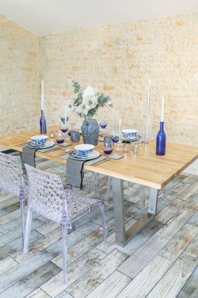 A rustic dining table with a natural wood surface serves as the base for French Country table decor, set with soft-toned tableware and understated linens.