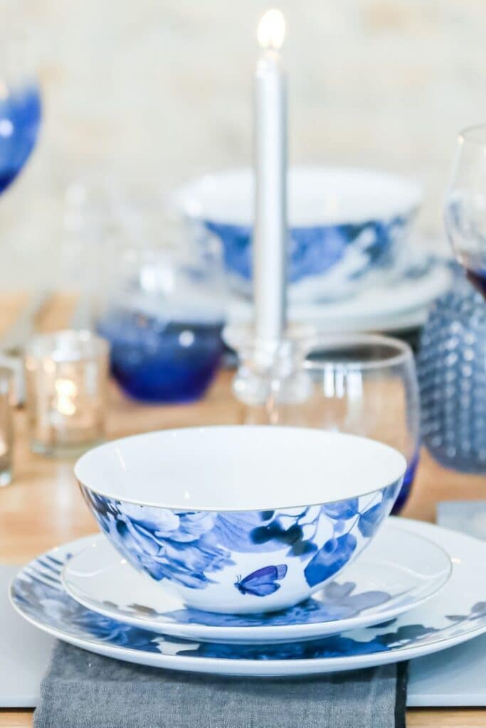 Close-up of a French Country table setting showing blue floral plates and bowls paired with ombre blue glassware and gray place mats for a cohesive yet contrasting look.