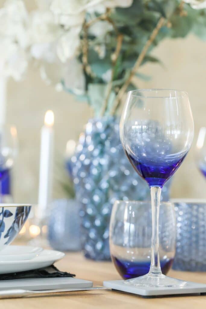 French Country dining table decorated with tall clear candlesticks, textured glass vases, and a soft floral centerpiece to create visual height and natural texture.