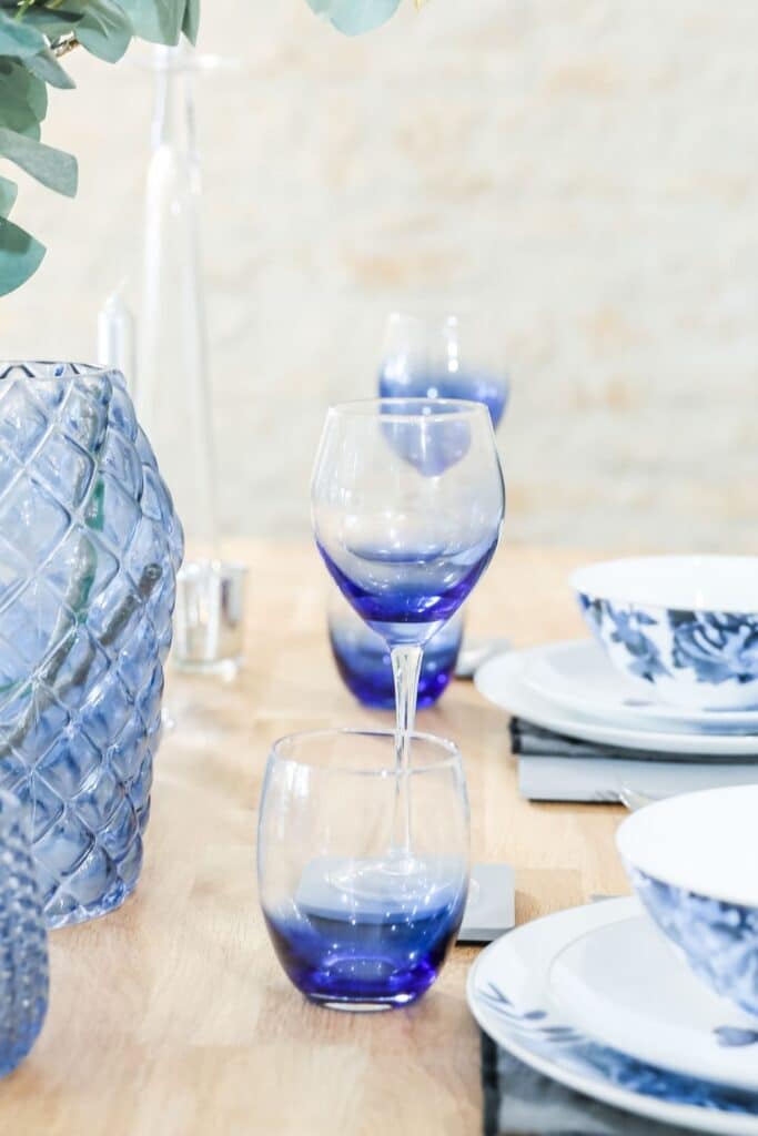Close-up of a textured blue glass vase with white faux flowers and eucalyptus branches, adding height and organic texture to the French Country table decor.