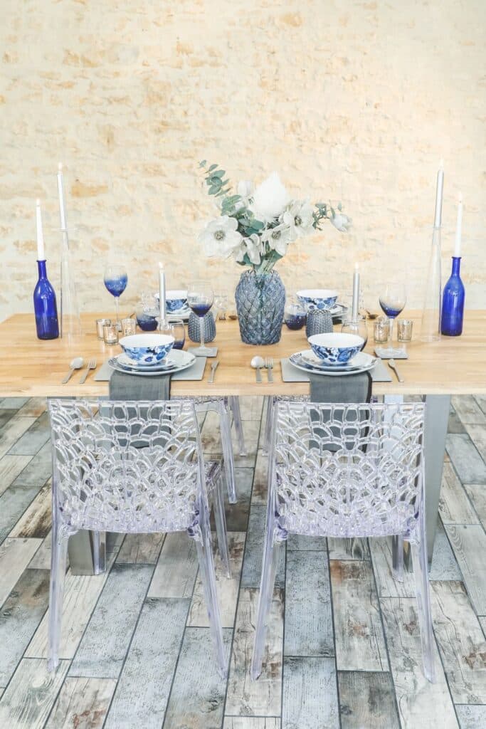 Transparent, patterned acrylic chairs add a modern yet elegant twist to the French Country table decor, blending seamlessly with the soft wood table and rustic stone walls.