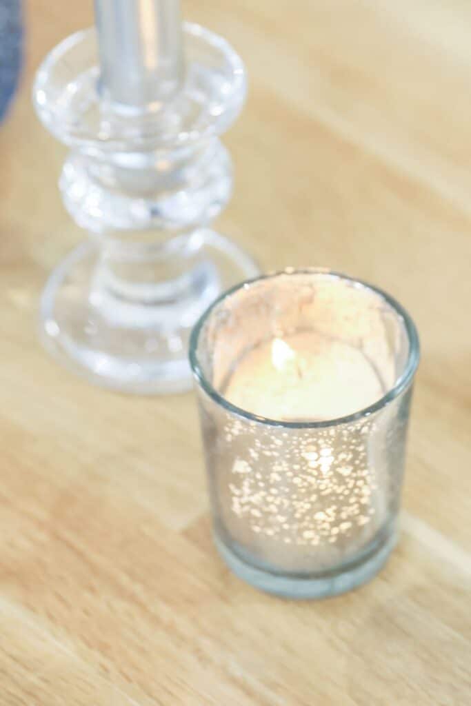 A close-up of a mercury glass votive with a lit tealight candle, casting a soft glow that enhances the cozy, romantic mood of French Country table decor.