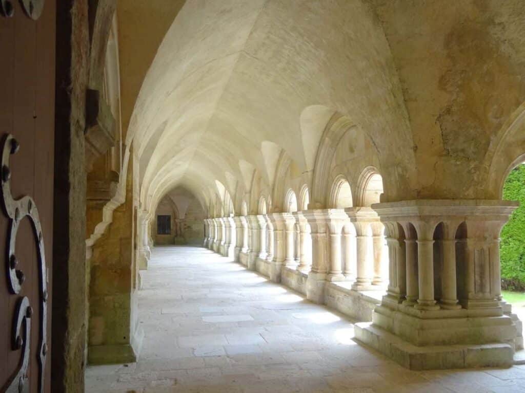Elegant arched cloister walkways inside Fontenay Abbey, with thick Romanesque columns and soft daylight illuminating the peaceful corridor.