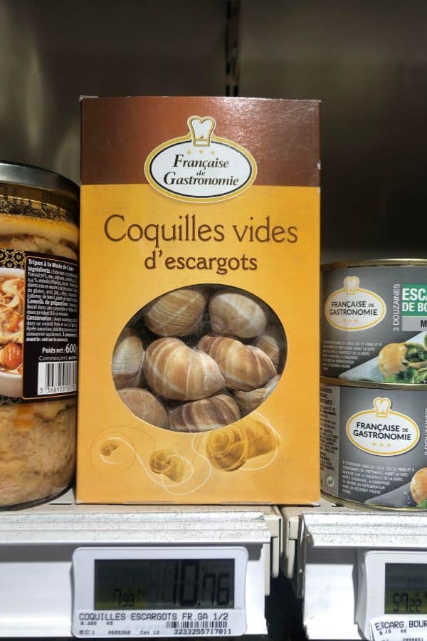 A supermarket shelf display featuring a box labeled “Coquilles vides d’escargots” from Française de Gastronomie, containing empty snail shells for escargot preparation. This product ties into the preparation process central to why the French eat snails.