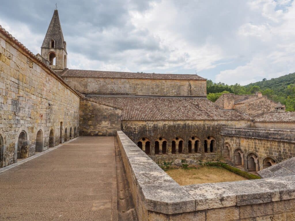 A view over the stone cloister garden and tiled roofs of Le Thoronet Abbey in southeastern France, showcasing its rustic Romanesque design and monastic simplicity.