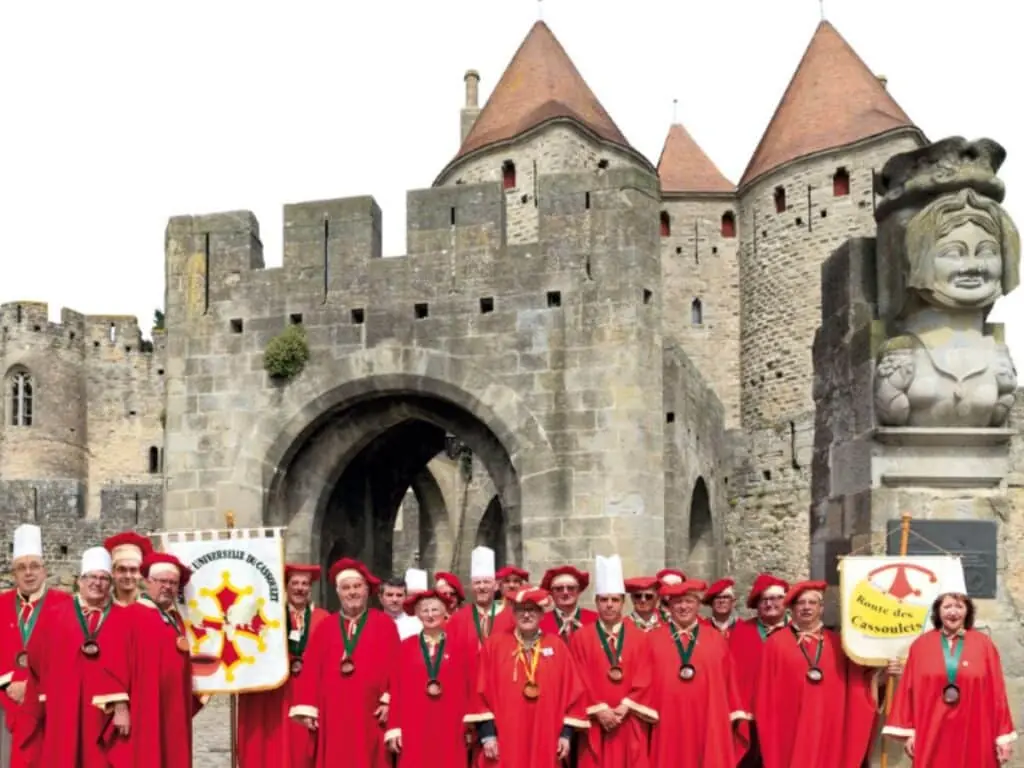 Members of the Cassoulet Brotherhood dressed in red robes gather at the historic gates of Carcassonne, celebrating the cultural and culinary heritage of cassoulet in southwestern France.